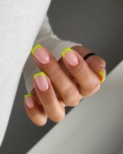 hort summer nails with bright neon yellow French tips and small orange dot accents on pink nail bed