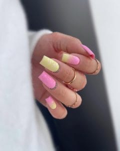 Long square July nails with alternating pink and yellow polish and rhinestone half moon accents at cuticles