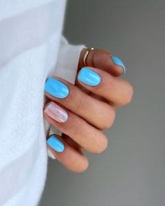 Short July nails with bright sky blue polish and one accent nail with gold lines and small blue flower details
