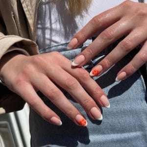 Long almond summer nails with nude base, white French tips, and small orange flower accent designs
