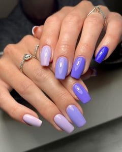 Long square July nails with purple ombre gradient from light lavender to deep royal purple across different nails
