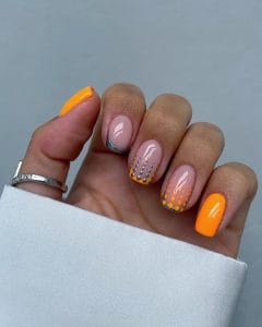 Short square July nails with nude pink base, silver French tips, orange accents, and silver dot gradient patterns