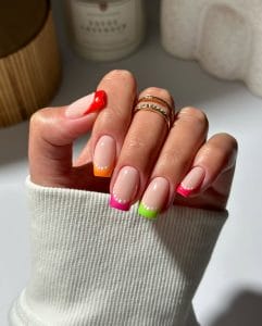 Long square July nails with nude base and colorful neon French tips with white dot accents
