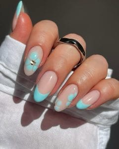 Long almond July nails with milky pink base and turquoise floral designs, French tips, plus small gold flower charm accent