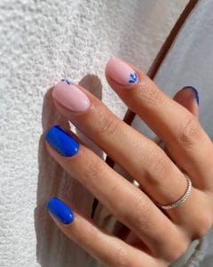 Short July nails with milky base, bright blue accent nails, and small blue flower designs